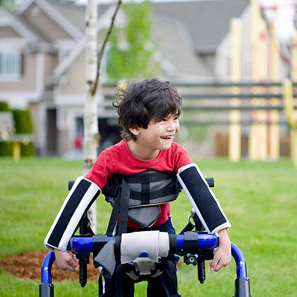 Disabled four year old boy standing in walker near a playground