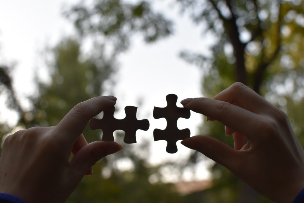 A pair of hands hold up two puzzle pieces, about to fit them together.