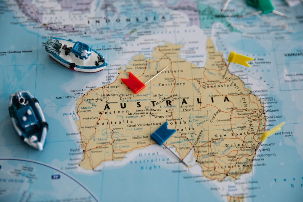 A picture of a map of Australia, with four flag pins and two model boats scattered on top of it.