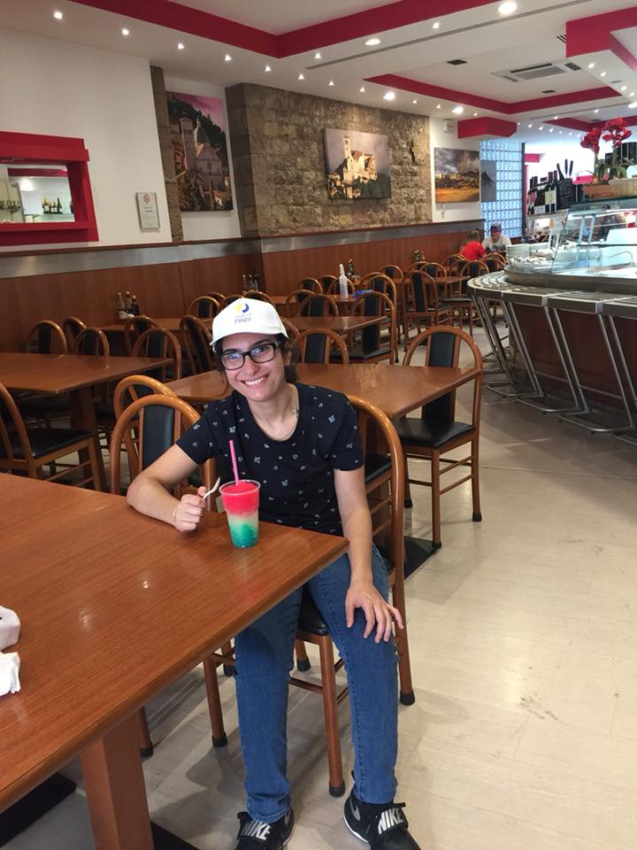 Cassandra sits in a restaurant with a colourful slushie on the table in front of her