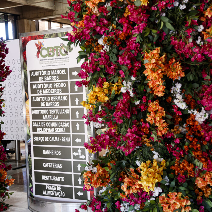 A photo from the host building at the Brazilian congress of occupational therapists. A CBTO standing sign points out directions to various places, next to a lush pillar of multicoloured flowers.